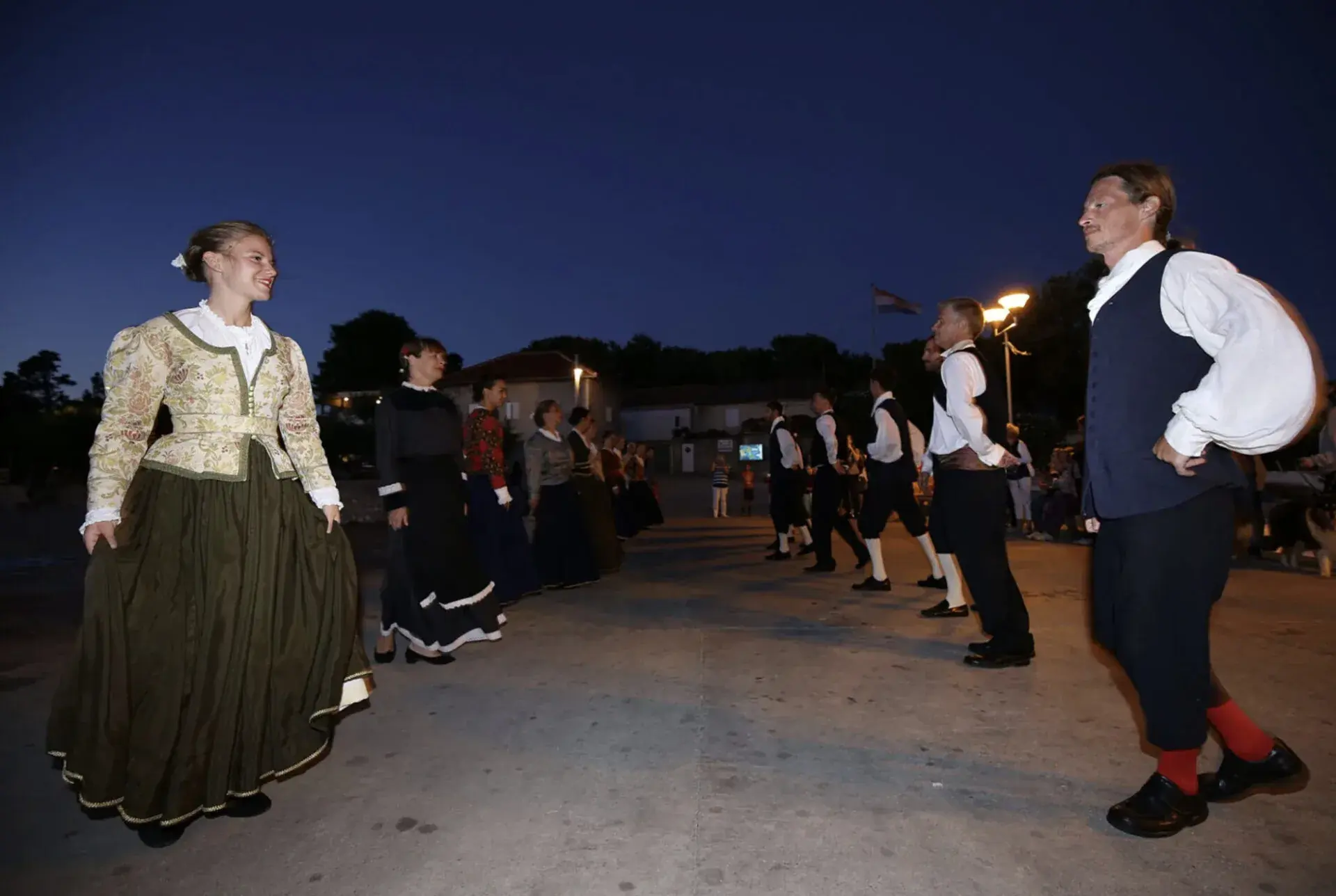 Plesni parovi u nošnjama plešu na trgu u Silbi u sumrak.