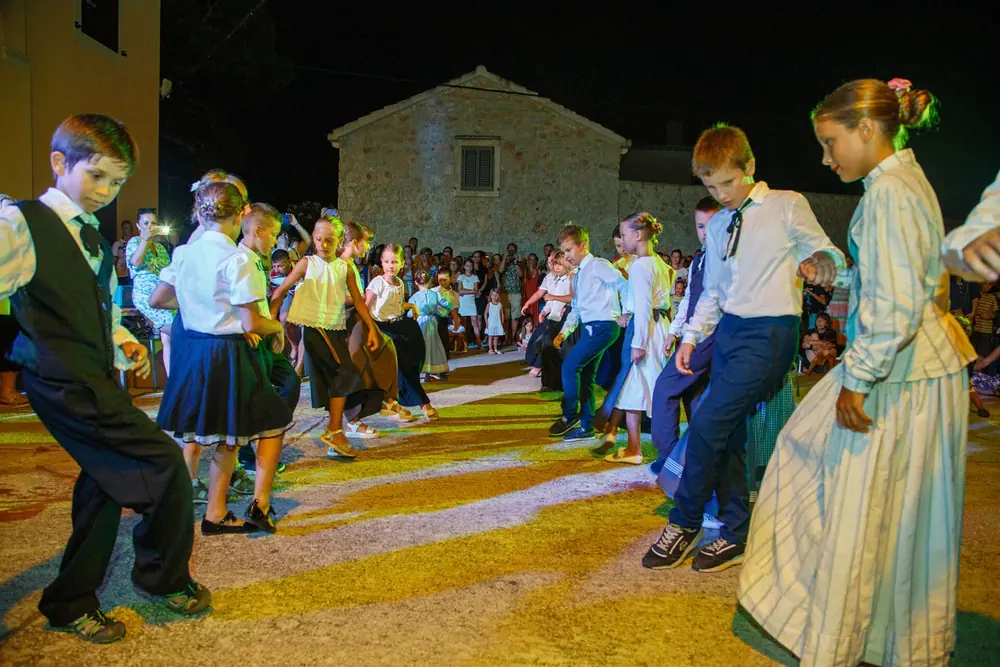 Djeca u nošnjama plešu u parovima na večernjoj priredbi.